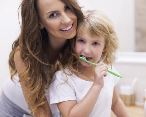 Mother helping daughter brush teeth